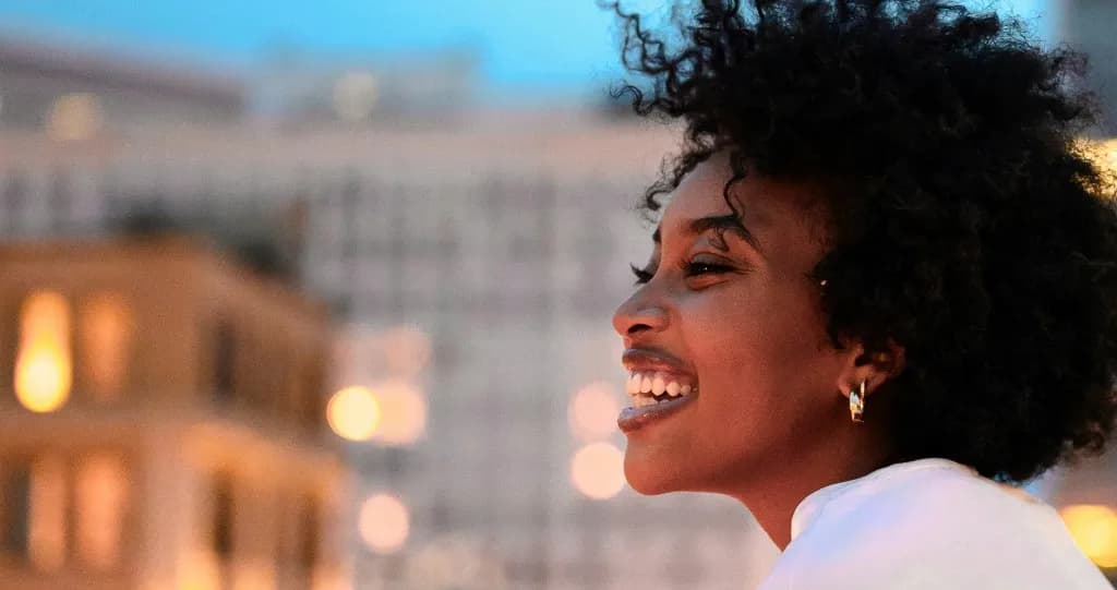Smiling woman with curly hair against a city skyline at dusk