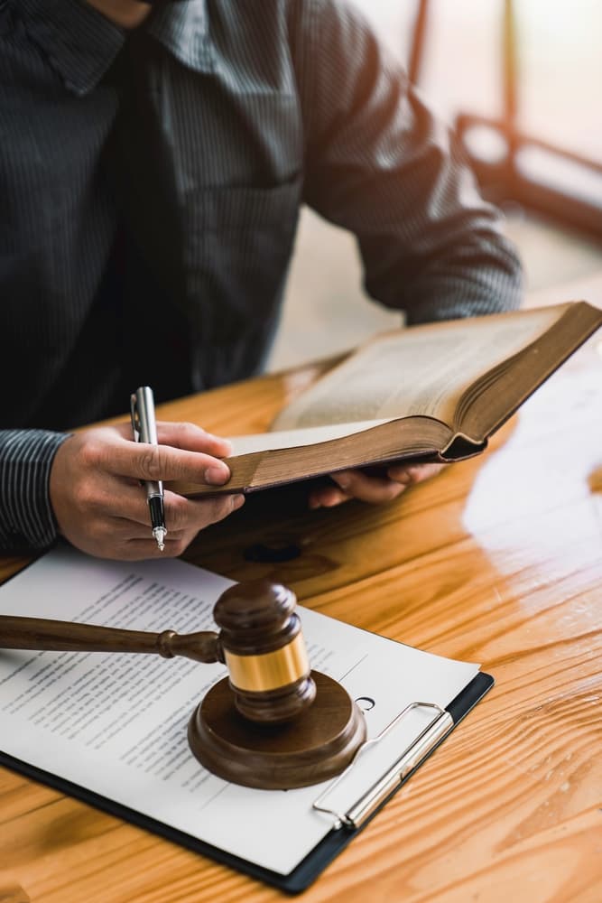 Focused attorney delving into legal codes, studying the constitution to safeguard human rights. Close-up of a male lawyer or judge working with law books and a gavel.