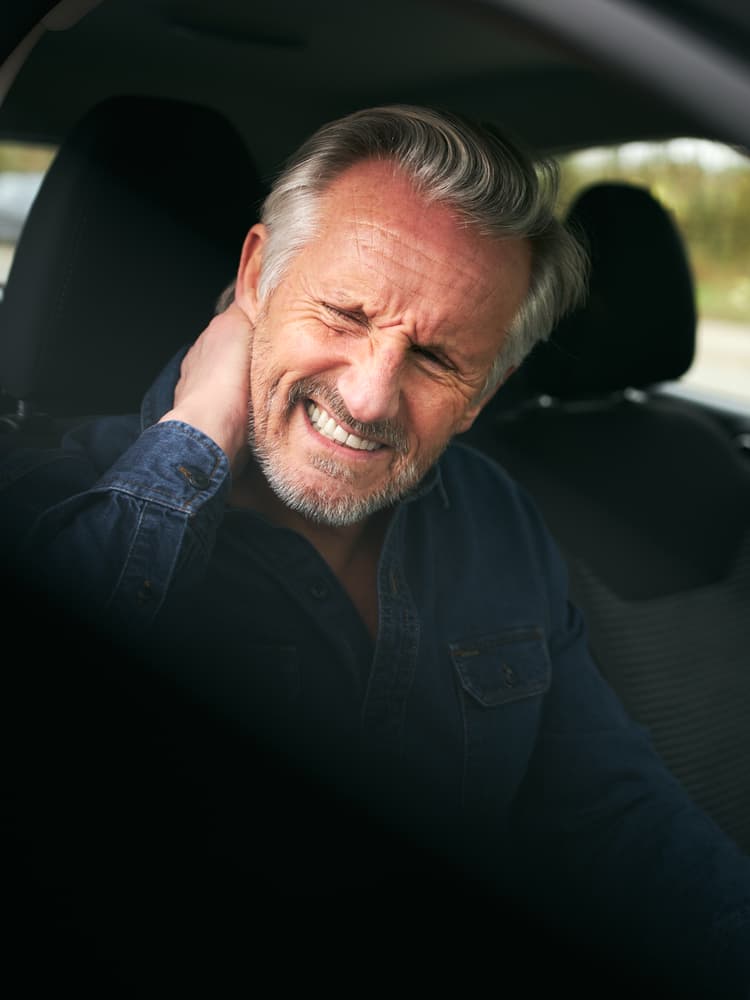 Elderly gentleman in car post-accident, experiencing pain and whiplash injury, seeking relief and support for recovery.