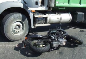 Wrecked black motorcycle on the asphalt following a collision with a cargo truck - aftermath of a road accident.