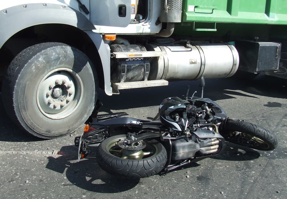 A damaged motorcycle lying under a large truck after a collision, illustrating a serious motorcycle accident scenario