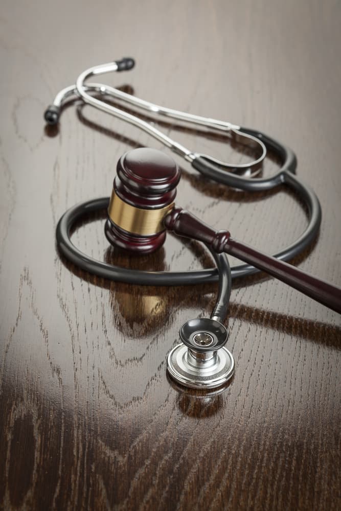 Legal and medical symbols: Gavel and stethoscope on a reflective wooden table, representing justice and healthcare in harmony.