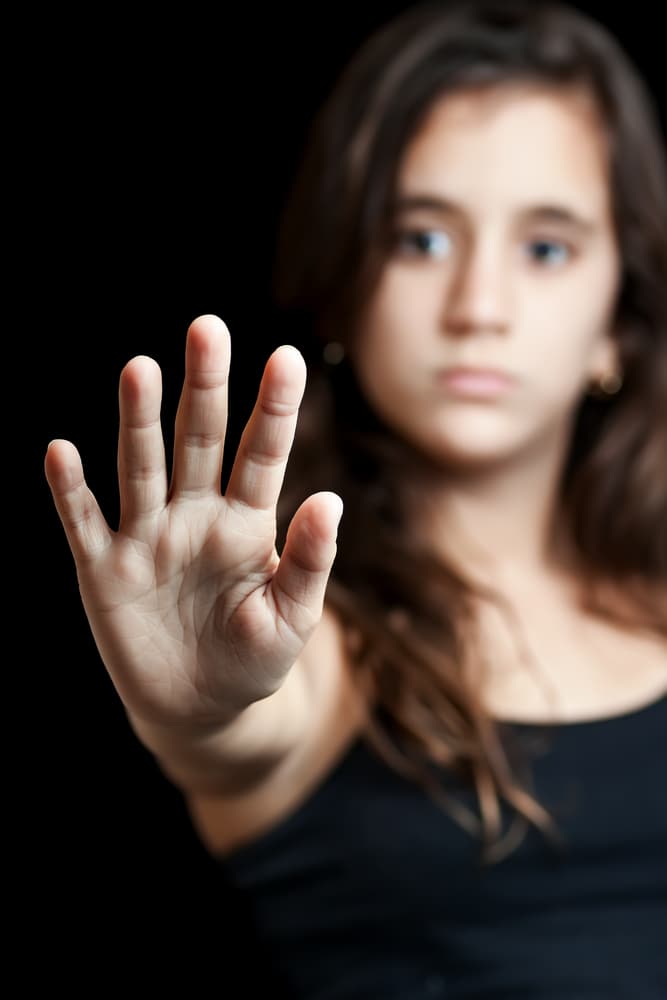 Young Latina advocating to end violence, gender, or sexual discrimination. Powerful image focused on her extended hand, signaling to stop. Join the campaign for change.