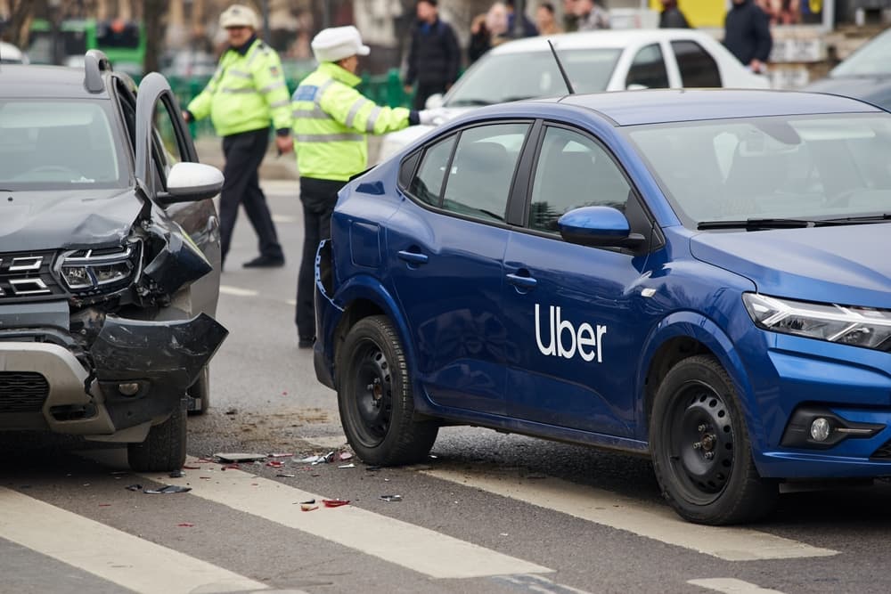 Two cars in a collision, one with Uber branding, and police officers on the scene assessing the accident.
