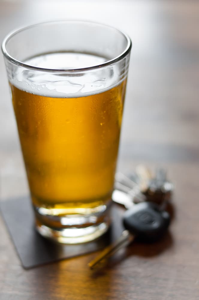 A glass of beer on a coaster with a set of car keys beside it, suggesting the dangers of drinking and driving.