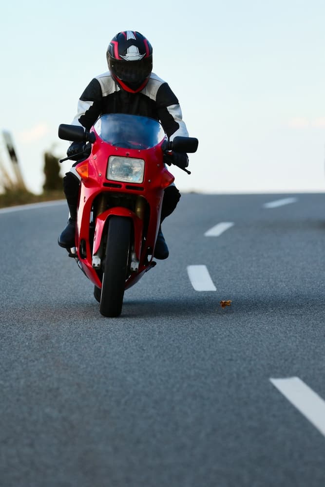 Front view of motorcyclist in leather gear riding a vibrant red motorcycle on the road with a slight tilt.