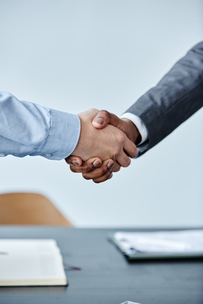 Close-up of two professionals shaking hands in a meeting, set against a clean blue backdrop, symbolizing a successful business agreement.