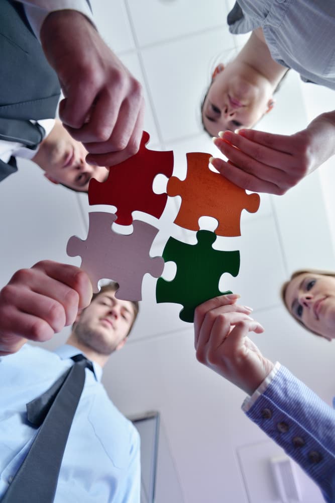 Four professionals collaboratively fitting together large puzzle pieces, symbolizing teamwork and problem-solving in a workplace