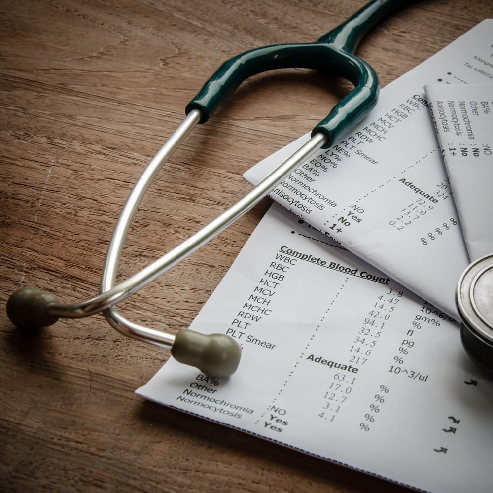 A stethoscope lies on top of a blood test report on a wooden surface.