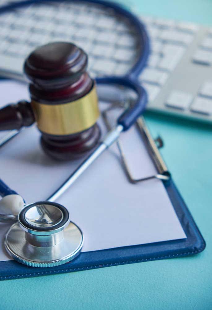 A gavel and stethoscope lies on a clipboard.