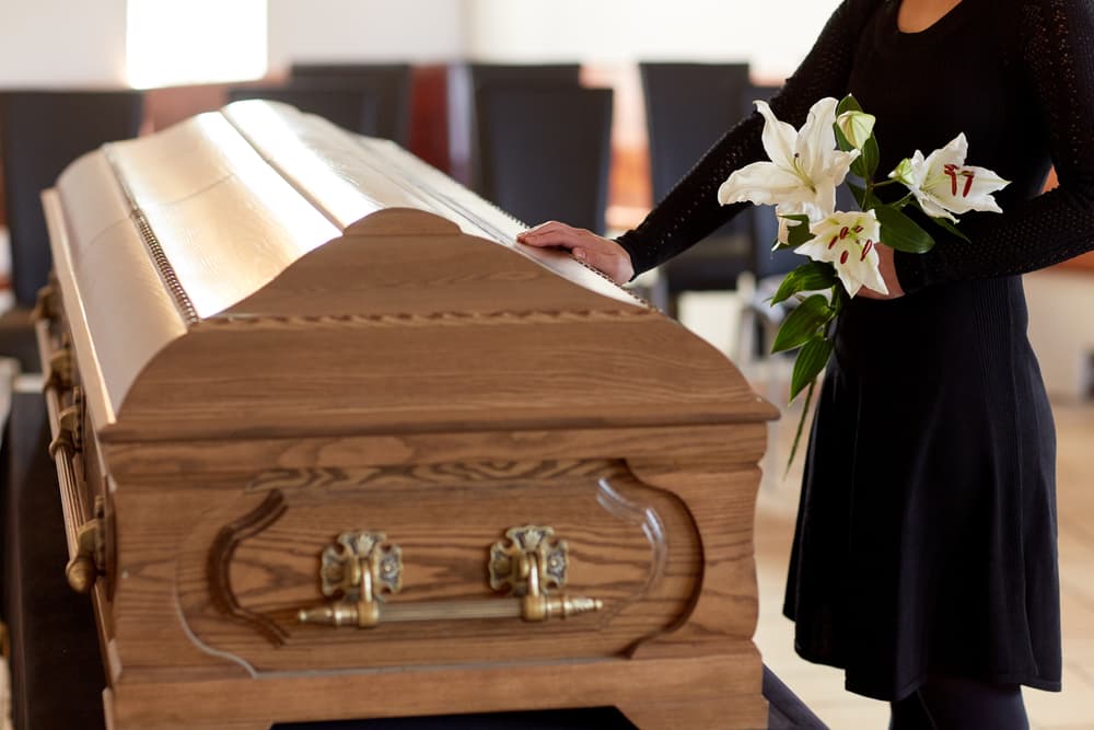 A woman next to a coffin with flowers in hand, at a service saying goodbye.