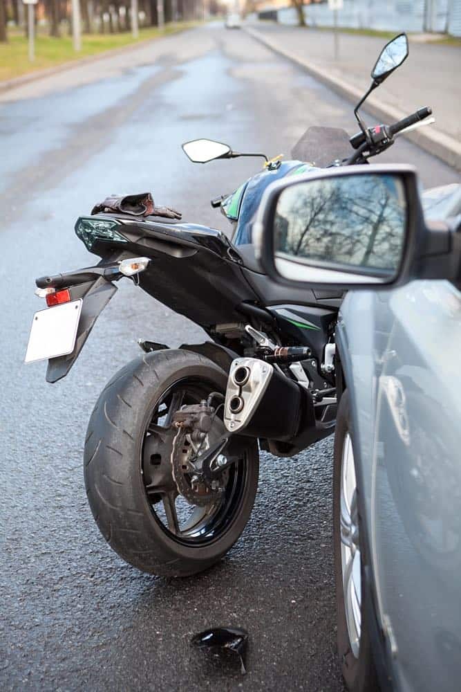 A black motorcycle damaged in a collision with a car on a wet city street