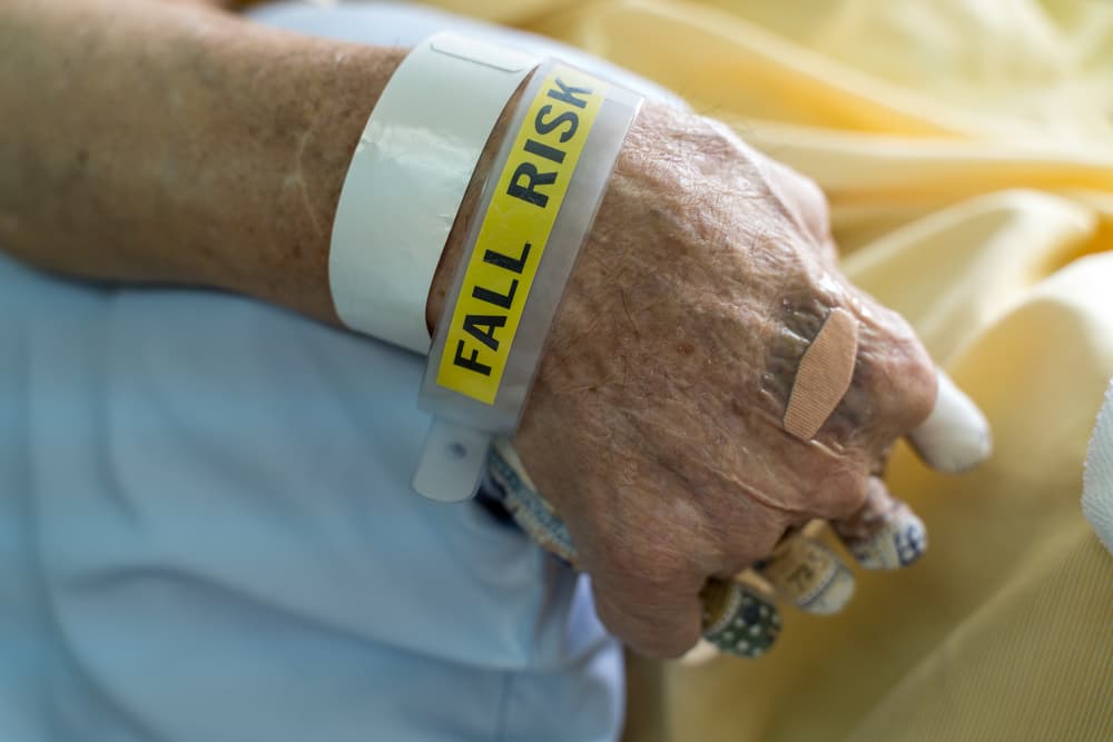 A hospital patient wears a fall risk bracelet and has a finger separation pad to prevent bedsores, commonly used for bedridden elderly patients.