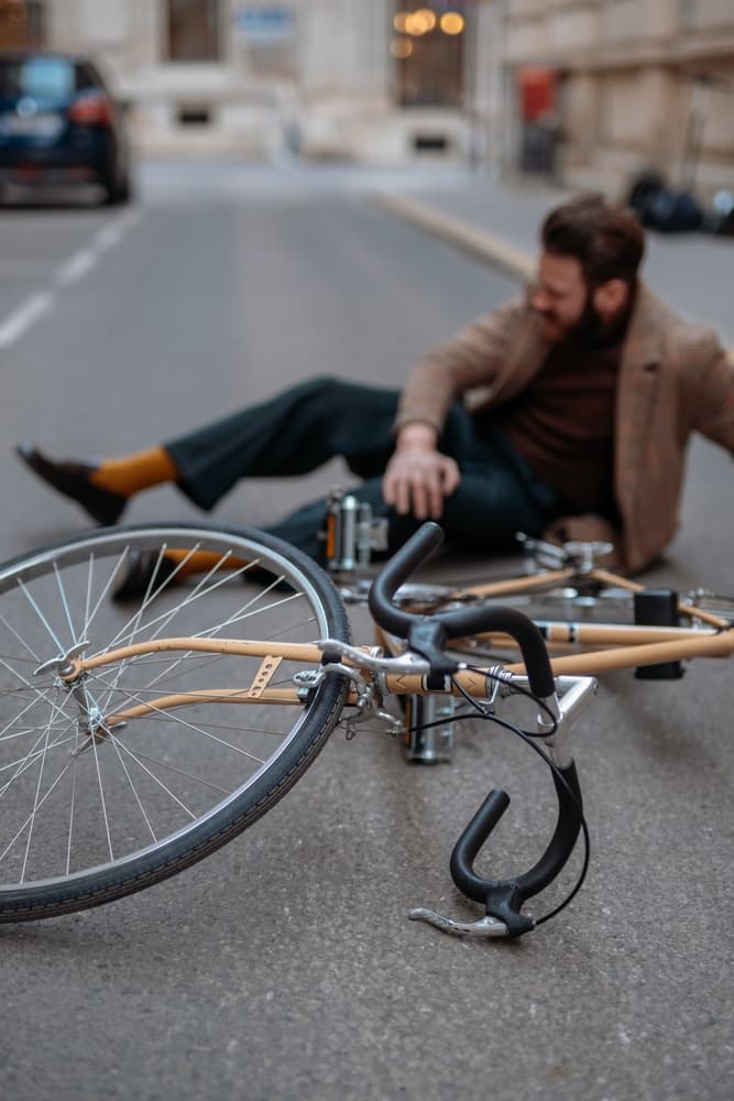 City bicycle accident: male cyclist falls off road bike while riding, suffering a knee injury.