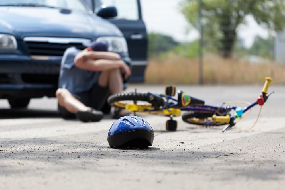 A boy in pain after being hit by a car while riding his bike.