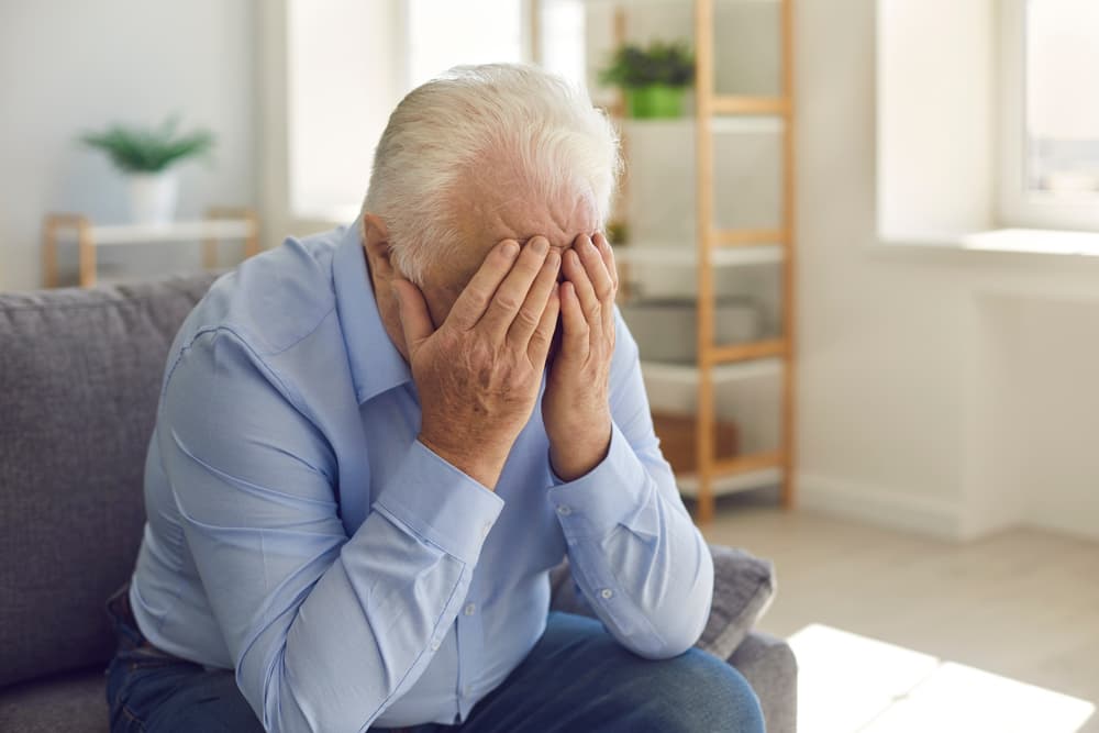 Distressed elderly man weeping, covering his face with his hands.