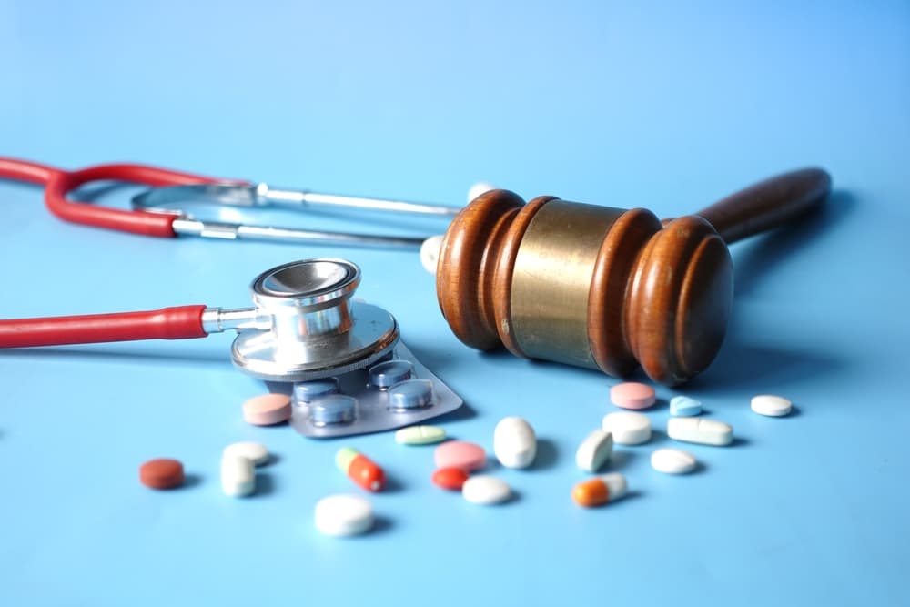 Flat lay of a gavel, stethoscope, and scattered pills on a blue background.