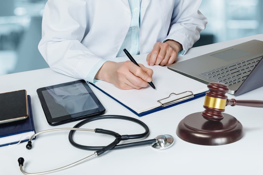 A doctor completes a legal document while seated at a desk in the office.