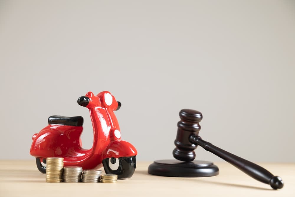 Close-up of a red motorcycle piggy bank with a judge’s gavel and money on a blank background. Concept for vehicle insurance, legal claims, or accident compensation.