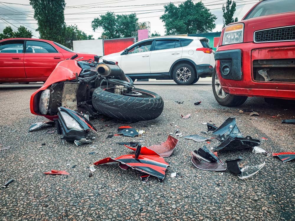 Motorcycle and car crash with a wrecked, broken bike left on the road.