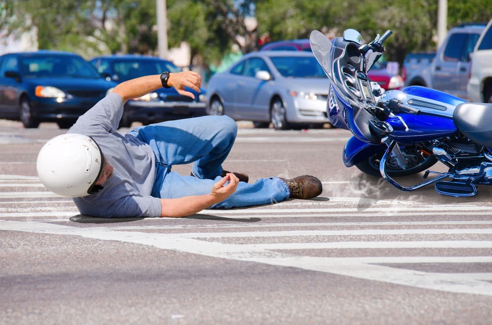 A motorcycle rider lies injured on the road as his bike slides across the pavement into a busy intersection.