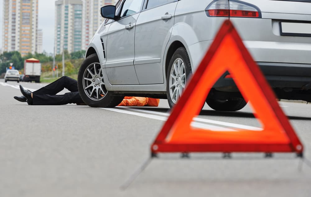 Pedestrian knocked down in road accident with distressed driver standing near crashed car after collision.