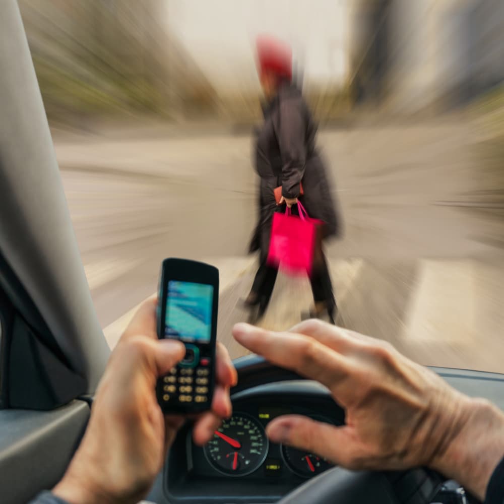 Blurred motion of a driver talking on a cellphone while speeding toward a pedestrian at a crosswalk.