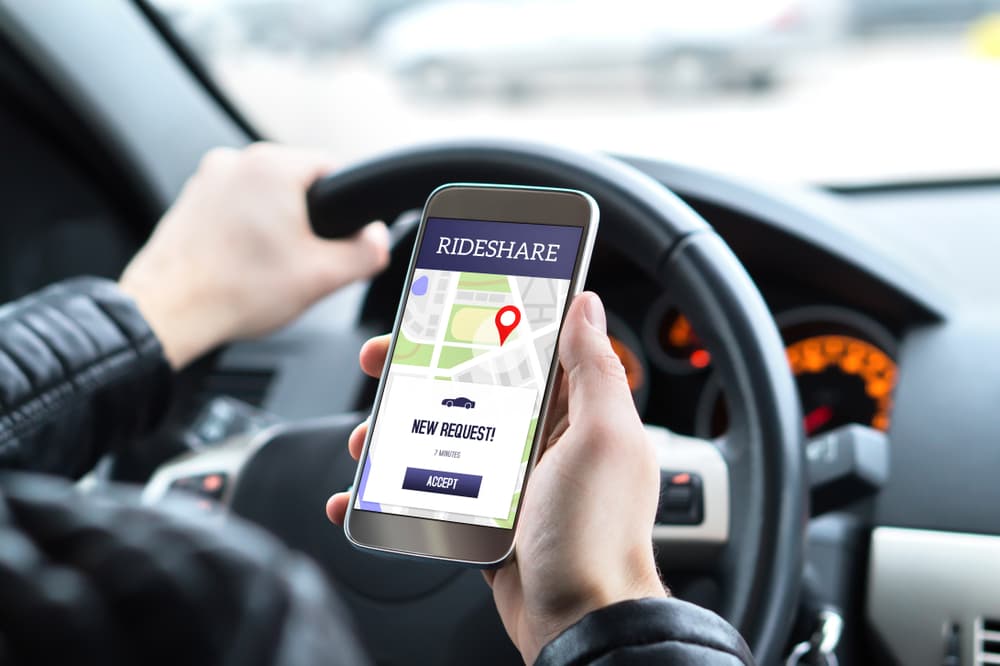Rideshare driver in a car using a smartphone app to accept a new ride request. Man picking up passengers through an online carpool service.