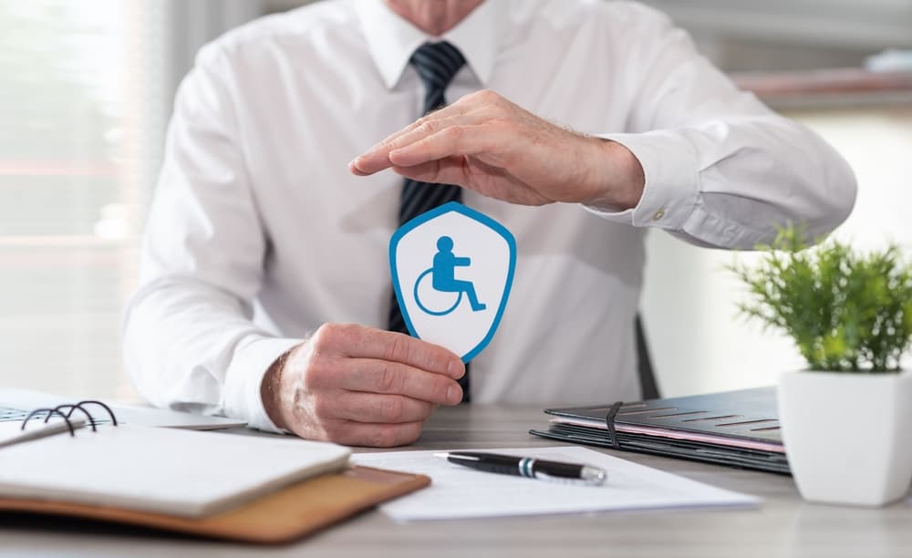 Concept of disability insurance illustrated by a paper shield being protected by the insurer’s hand.