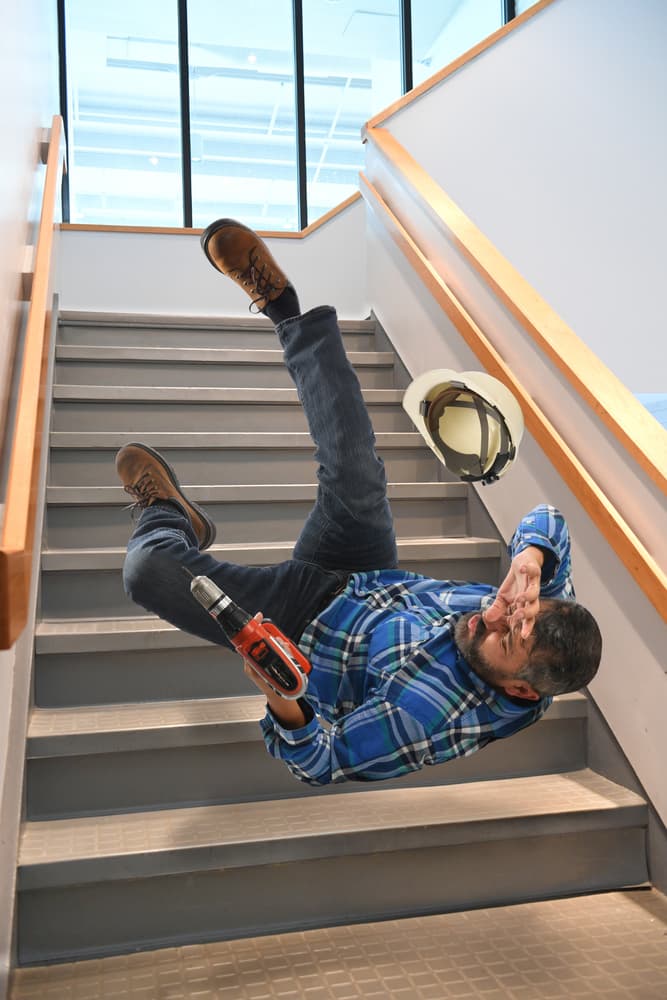 Older worker trips on stairs while carrying a cordless drill.