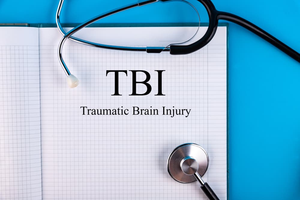 Notebook on a desk with "TBI" written inside, alongside a stethoscope—symbolizing the medical and legal challenges of traumatic brain injuries.