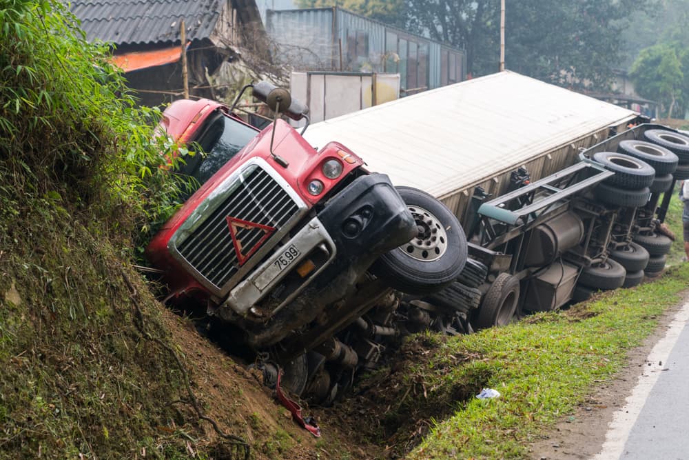 Motor vehicle accident on a mountainous road: a long vehicle overturned and lies in a ditch on the roadside after a serious car wreck.