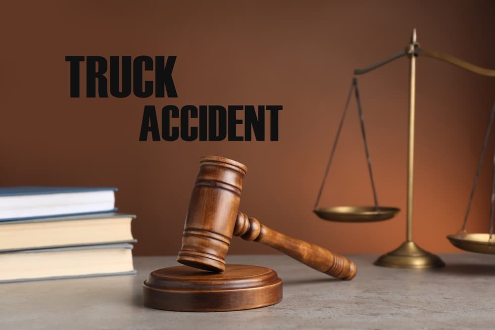 Truck accident law concept. A judge’s gavel, scales of justice, and legal books rest on a table with a brown background.