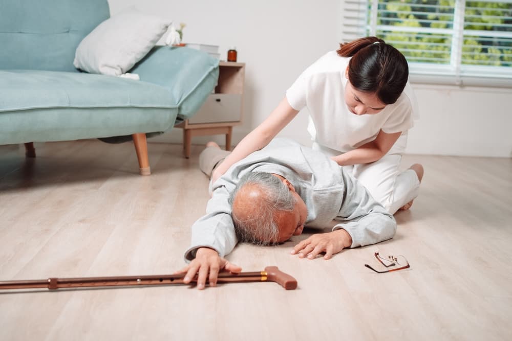 A woman helping senior male from falling on the ground in living room at nursing home.