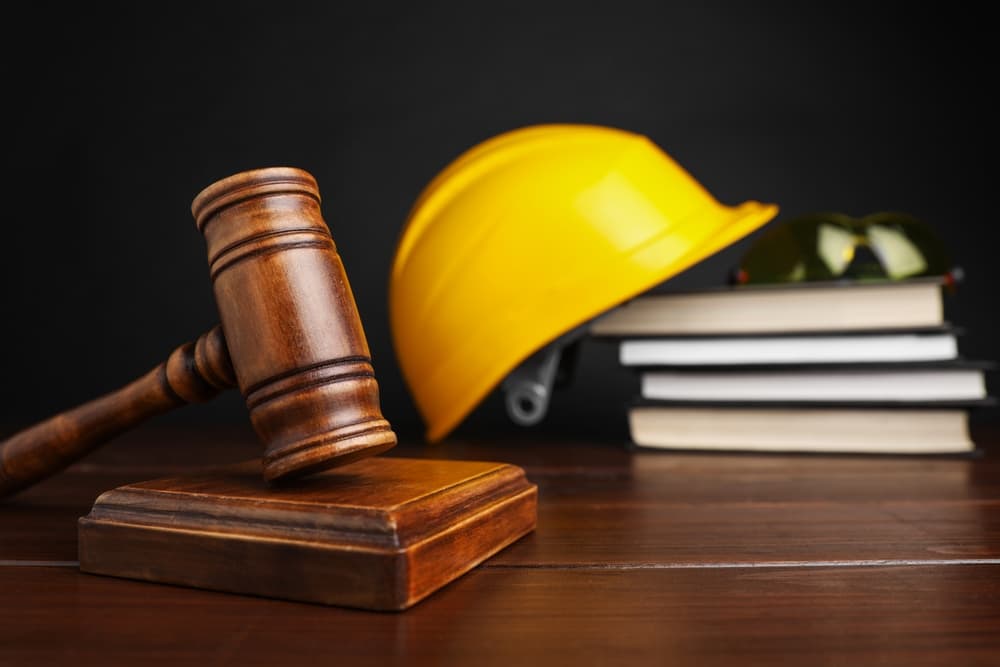 Workplace accident concept. Gavel, legal books, and construction safety gear on a wooden table, selectively focused for emphasis.